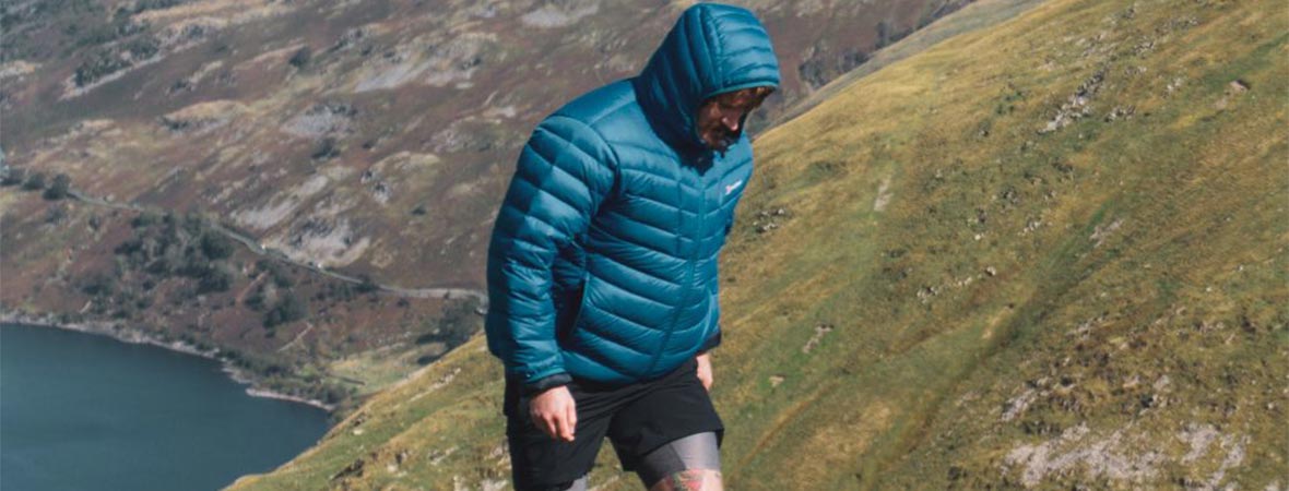 Man walking up a hill in a valley wearing a blue puffer jackets and shorts.