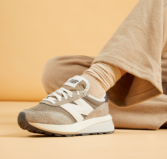 Seated model wearing ecru toned New Balance running trainers.