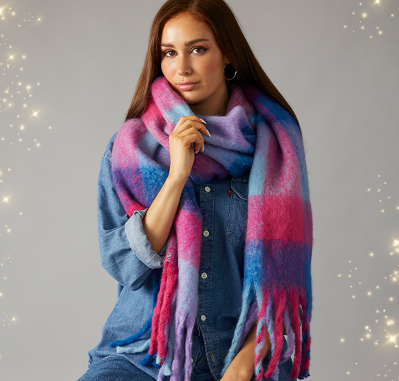 Female Model wearing a vibrant oversized French Connection scarf with a pink, purple and blue pattern with fringed ends.
