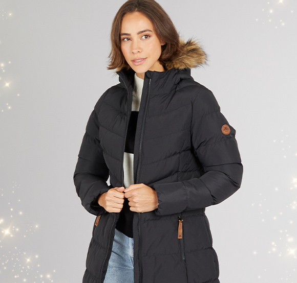 Long black Trespass winter coat with a fur-trimmed hood, modeled by a woman wearing light jeans.