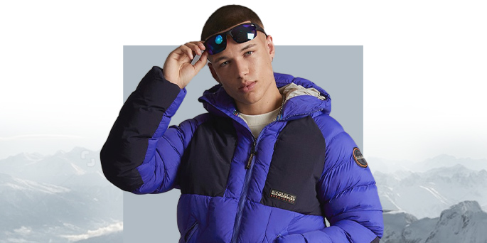 Male in a royal blue and black Napapijri puffer jacket with a hood, featuring black panels, adjusting his sunglasses.