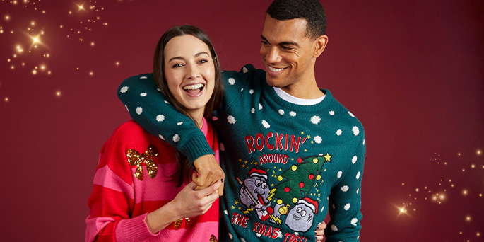 Smiling couple wearing Christmas jumpers. Woman in striped sweater with sequin bow. Man in polka dot jumper with festive logo.