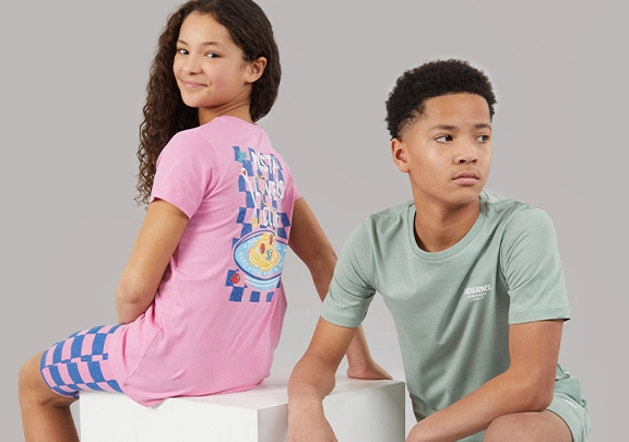 Girl in pink 'Pasta Lovers Club' t-shirt and checkered shorts next to a boy in a sage green t-shirt and matching shorts.